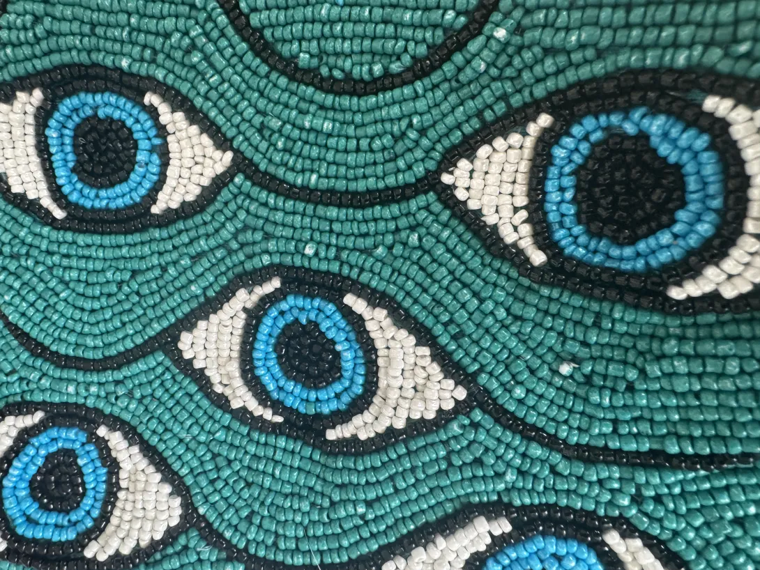 Beaded pattern of blue eyes on a teal background.